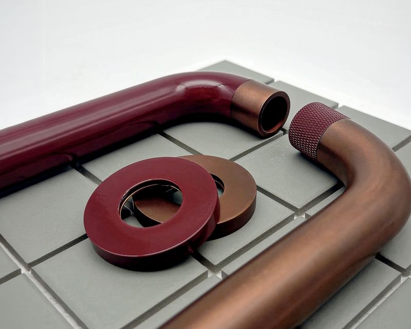 Custom finished tapware parts in burgundy and brushed copper, with a knurled collar, on green tiles